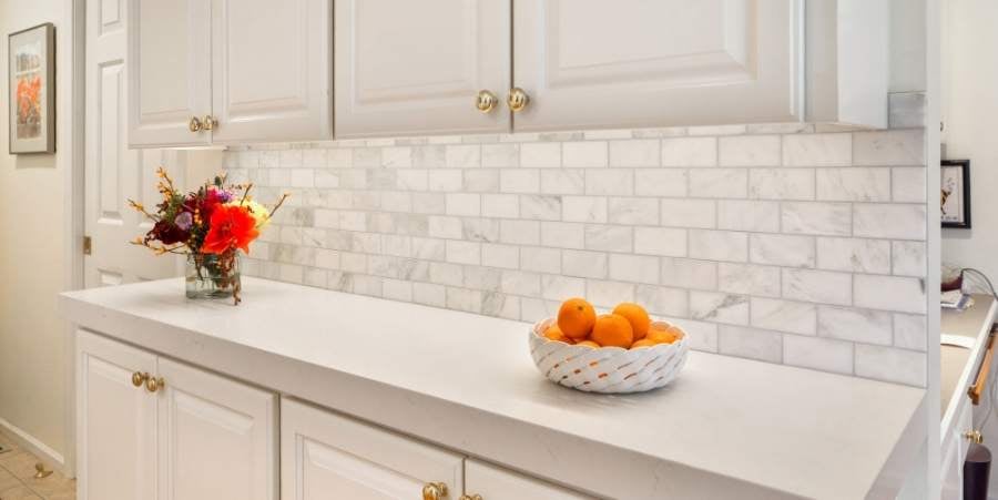 White counter with white tile with gold accents.