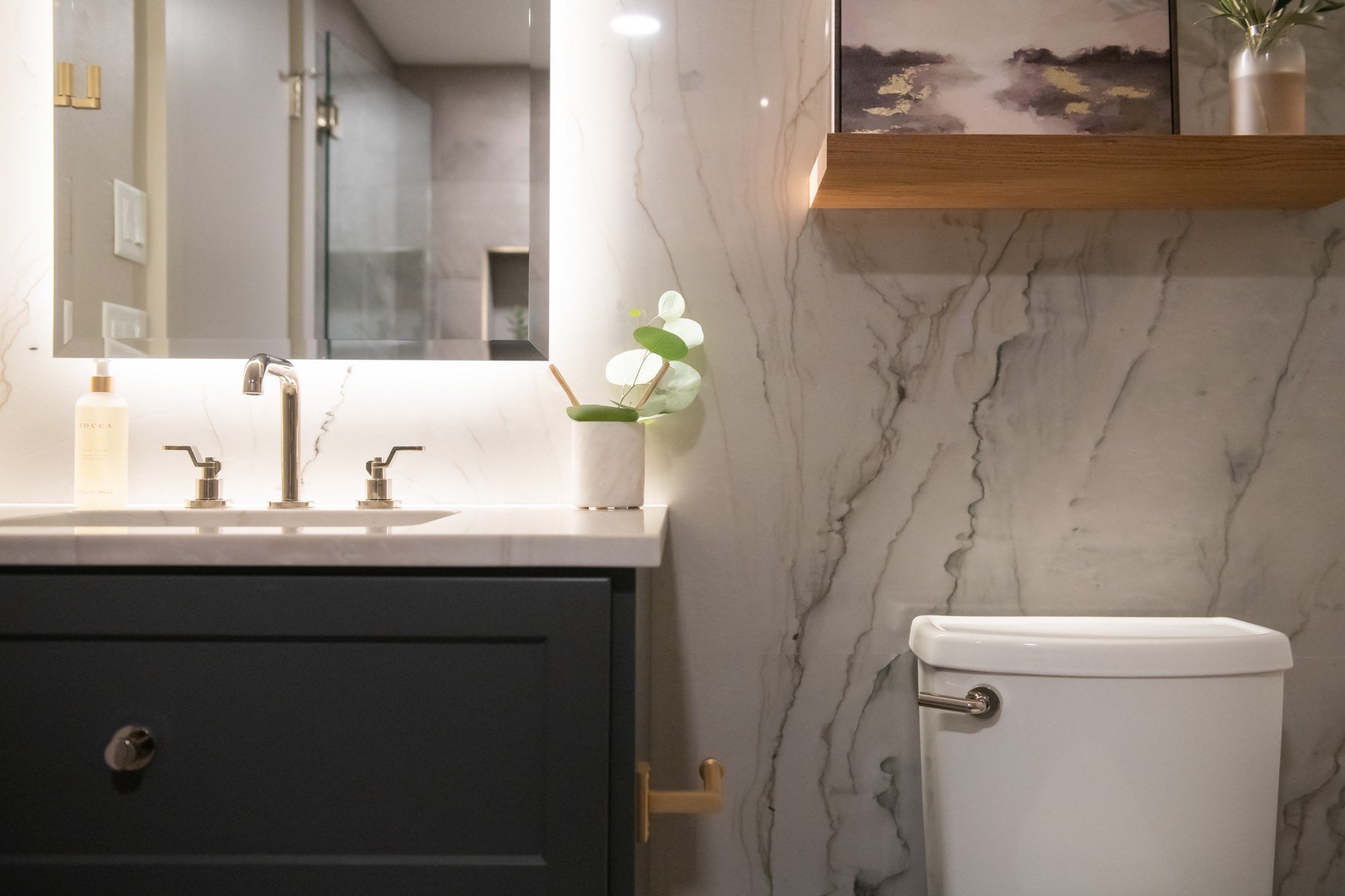 Marbled walls with dark grey vanity and backlit mirror in custom bathroom Marbled walls with dark grey vanity and backlit mirror in custom bathroom