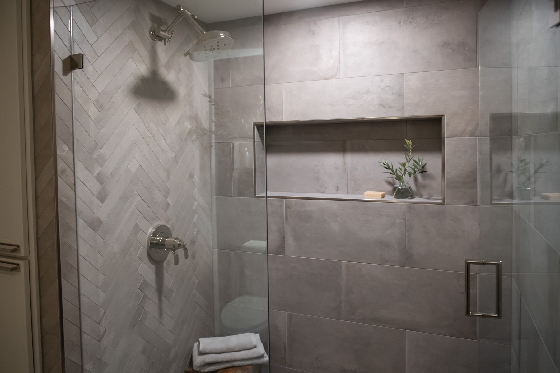 Walk-in shower with grey tile, shower niche, and glass doors Walk-in shower with grey tile, shower niche, and glass doors
